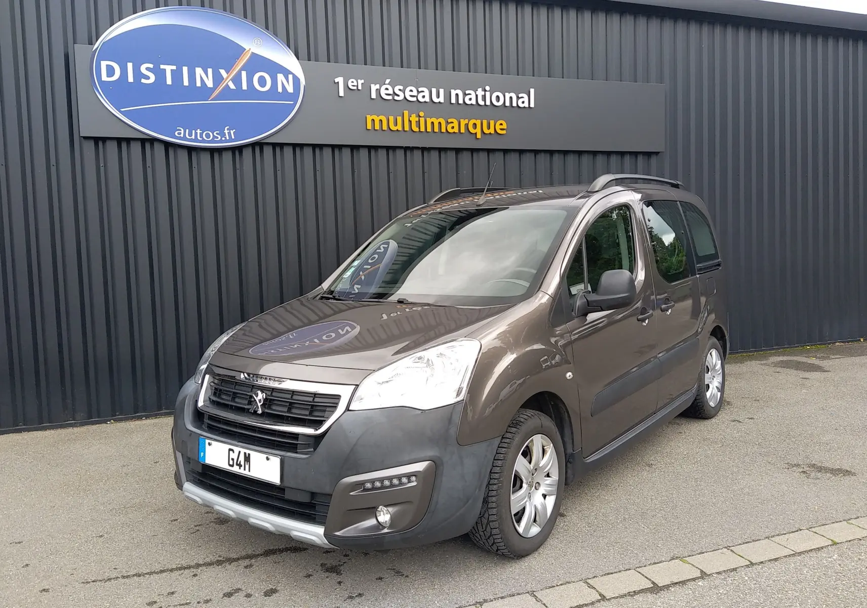 Peugeot Partner Tepee HDI 110 brun en 3/4 avant droit, avec barres de toit et pare-chocs noir mat visible.