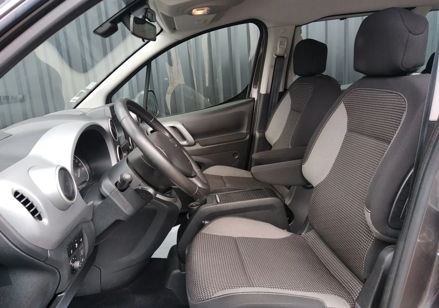 Intérieur avant du Peugeot Partner Tepee brun, vue côté conducteur montrant sièges tissu et tableau de bord gris.