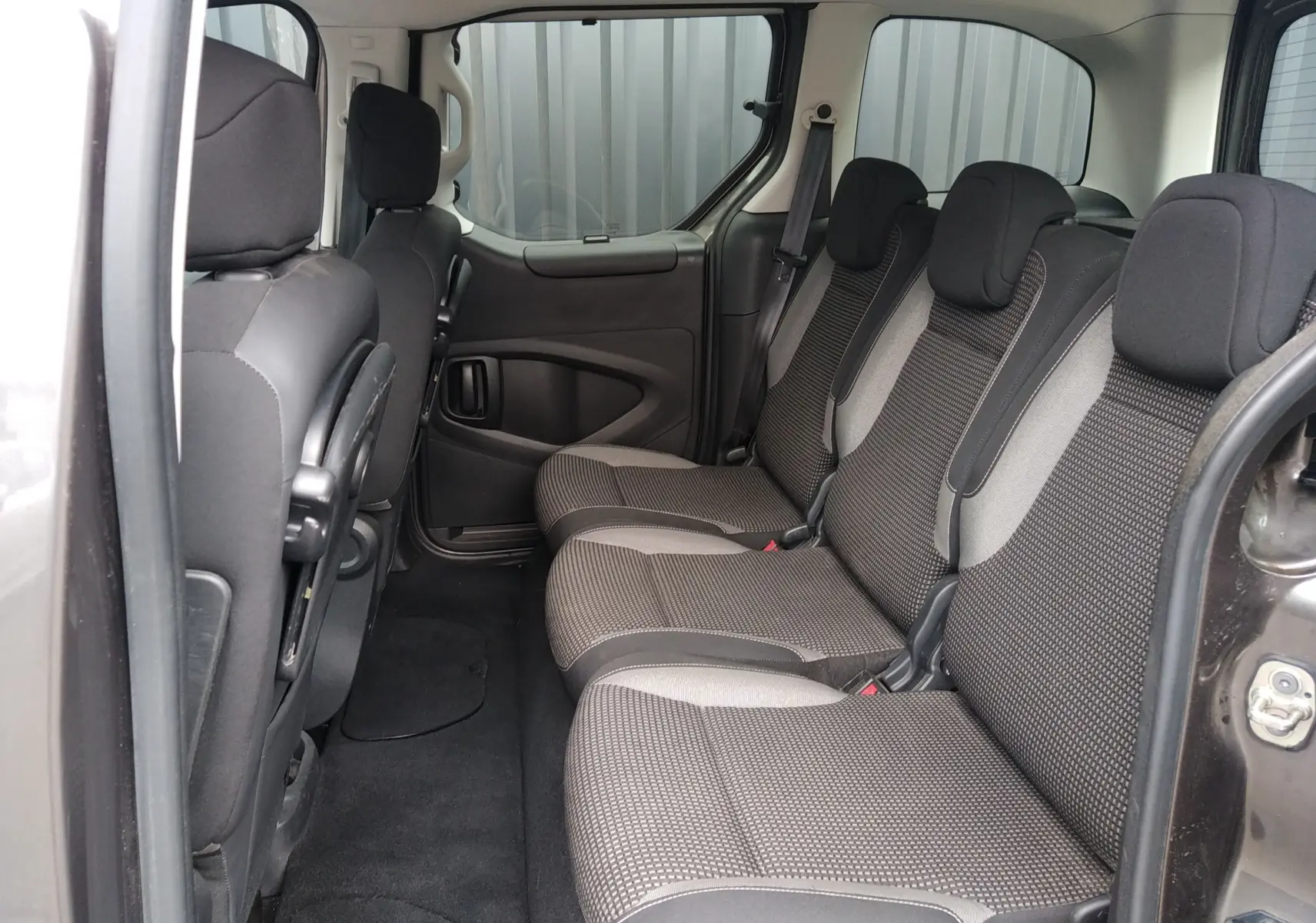 Vue intérieure côté droit des sièges arrière en tissu gris du Peugeot Partner Tepee brun, avec porte coulissante ouverte.