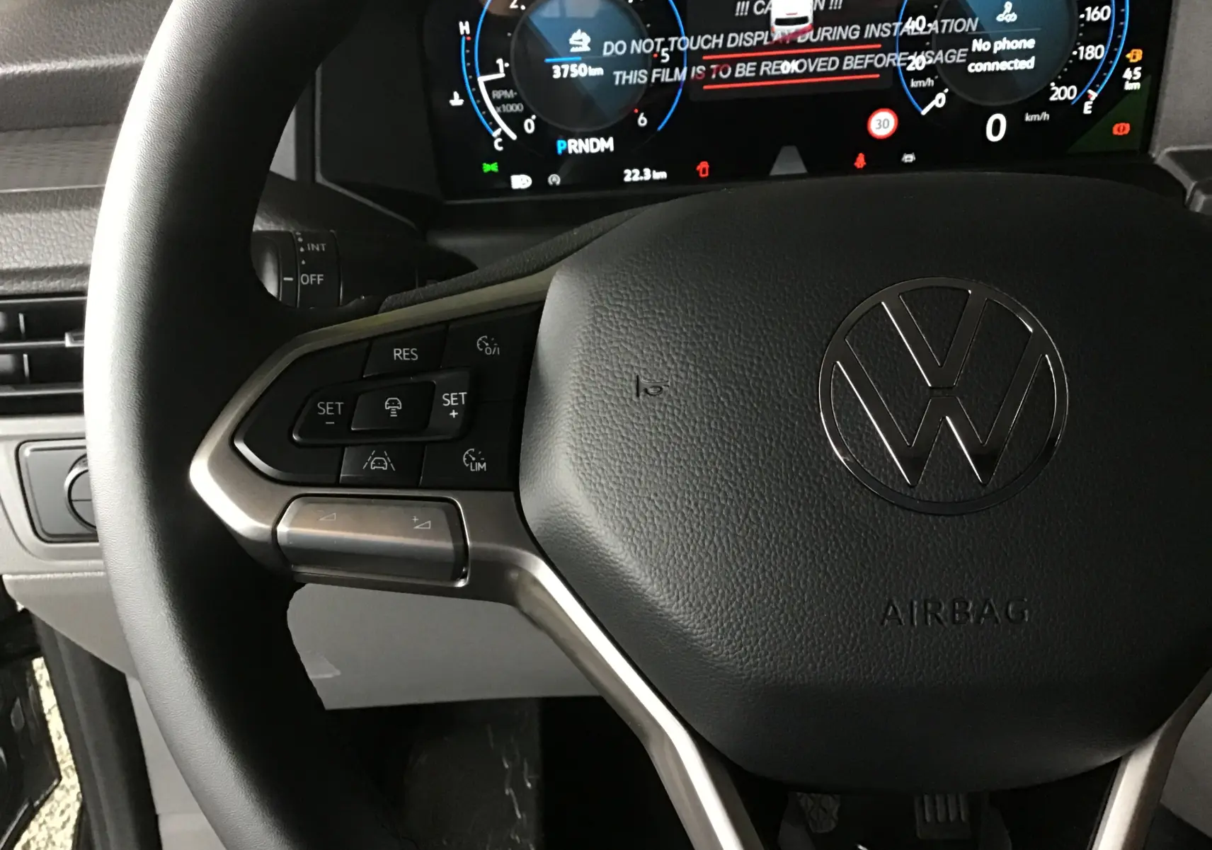 Gros plan sur le volant noir du Volkswagen Transporter T7 avec commandes intégrées et tableau de bord numérique en arrière-plan.