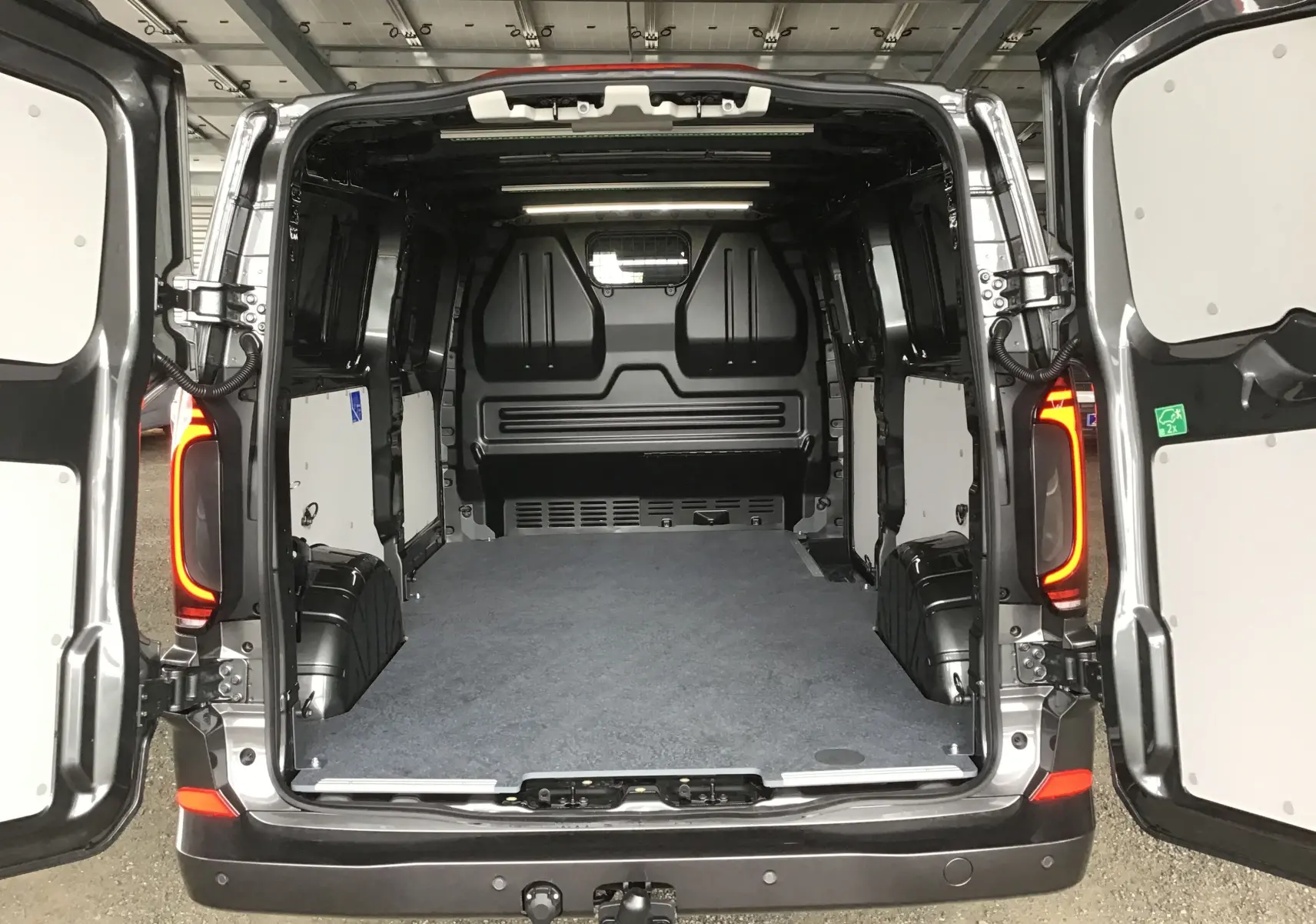 Vue arrière du Volkswagen Transporter T7 gris anthracite avec portes ouvertes montrant l'espace de chargement vide et le plancher recouvert.
