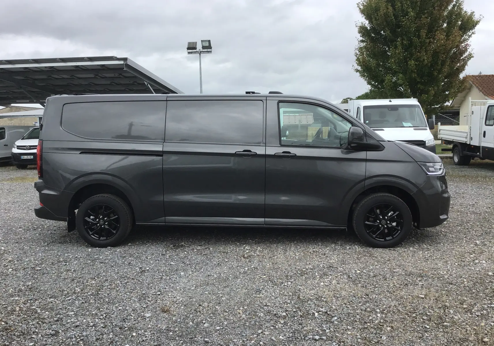 Profil côté droit du Volkswagen Transporter T7 gris anthracite avec jantes noires et barres de toit repliables.