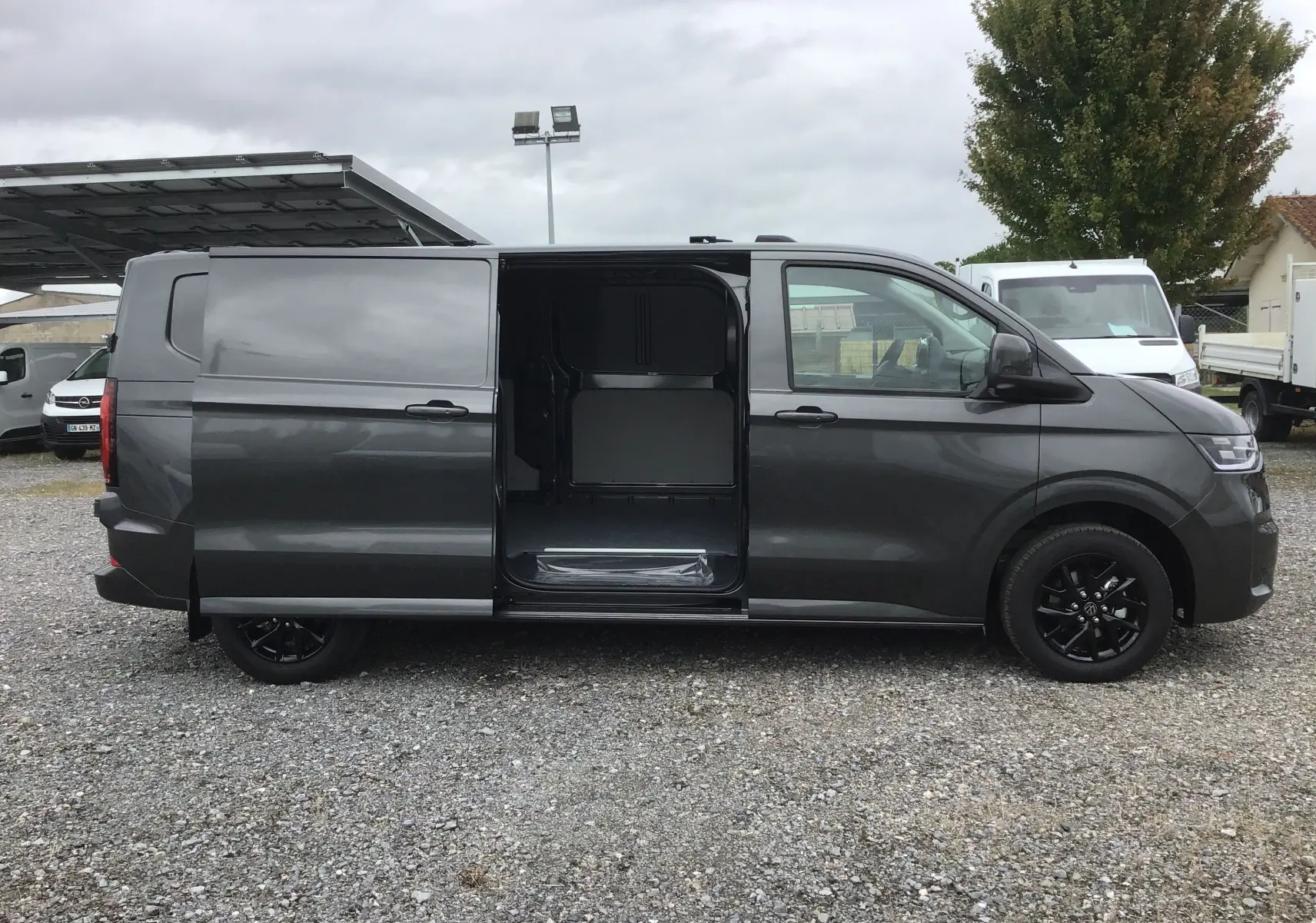 Vue latérale droite d'un Volkswagen Transporter gris anthracite 2025 avec porte coulissante ouverte et jantes noires.