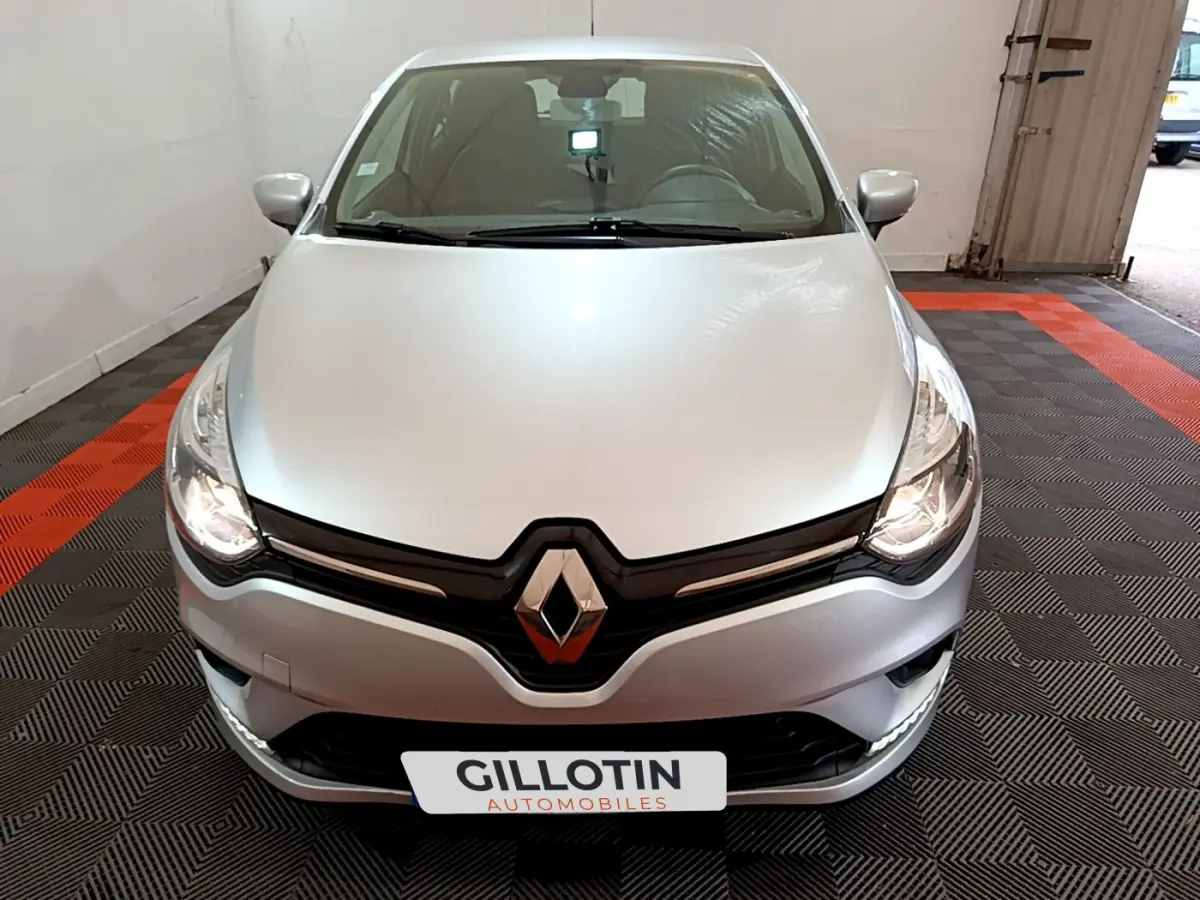 Renault Clio Business TCe 90 gris clair vue de face dans un garage avec phares allumés et logo Renault visible.