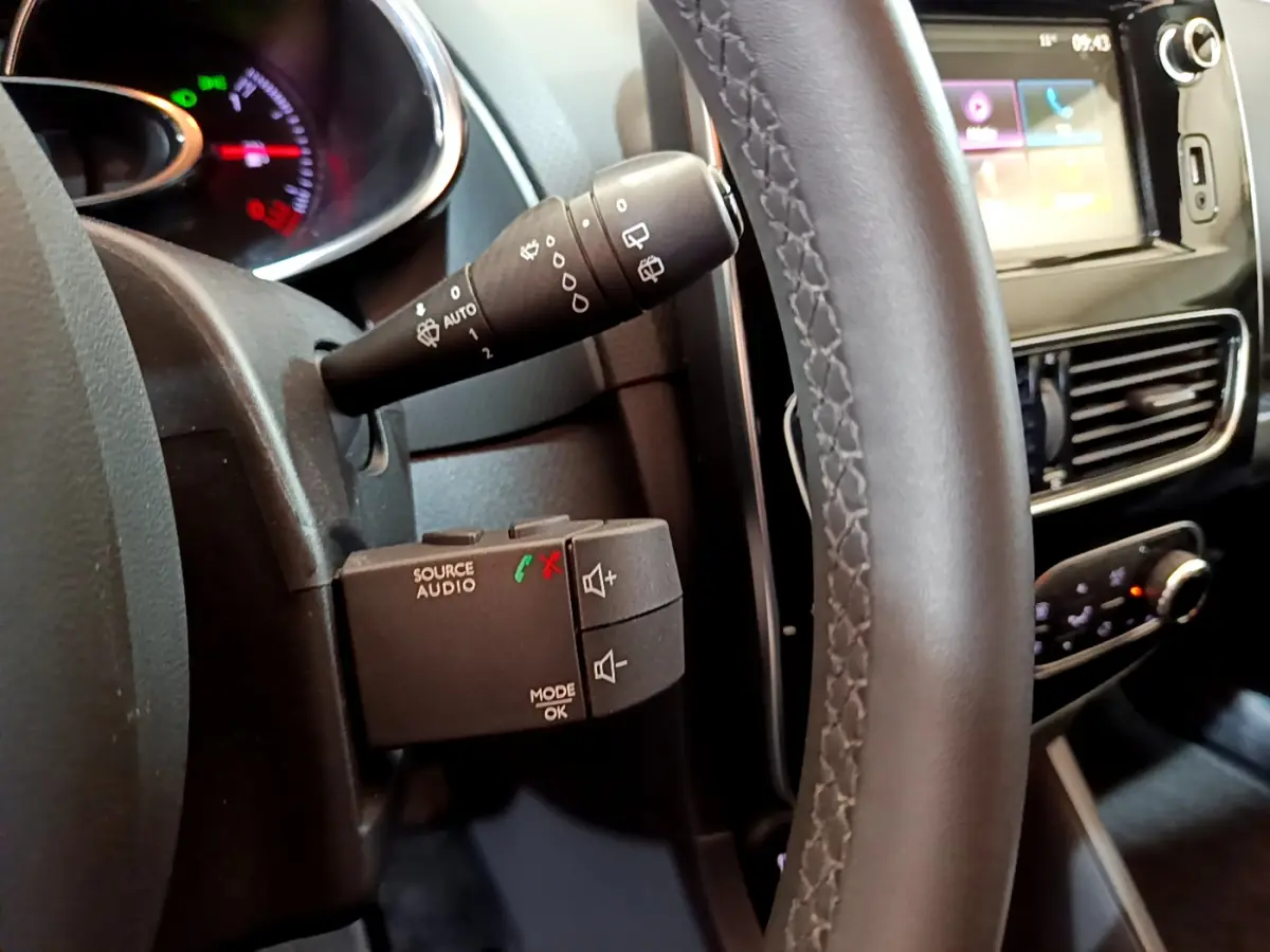 Gros plan sur le volant cuir et commandes audio au volant de la Renault Clio Business gris clair, avec écran tactile visible.