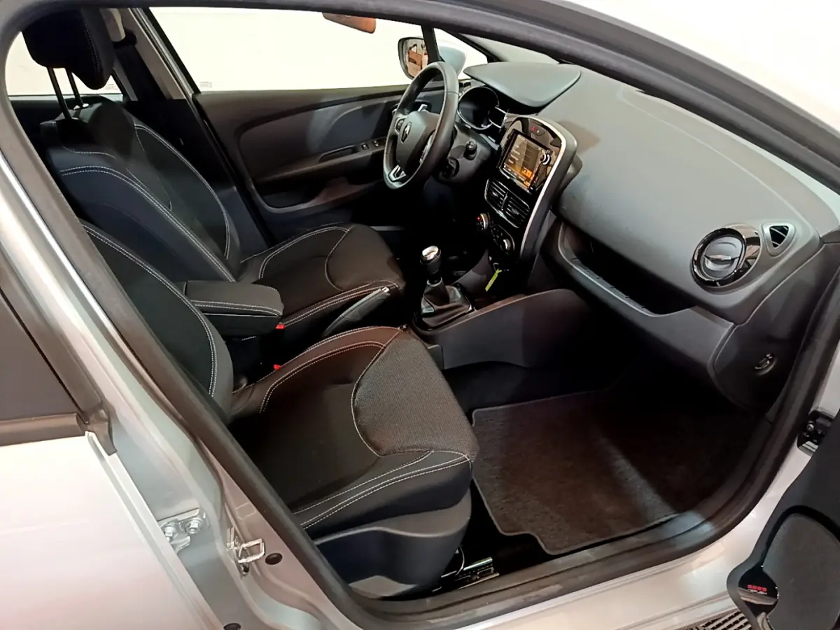 Intérieur de Renault Clio Business TCe 90 gris clair, vue côté conducteur, sièges noirs avec coutures blanches et tableau de bord moderne.