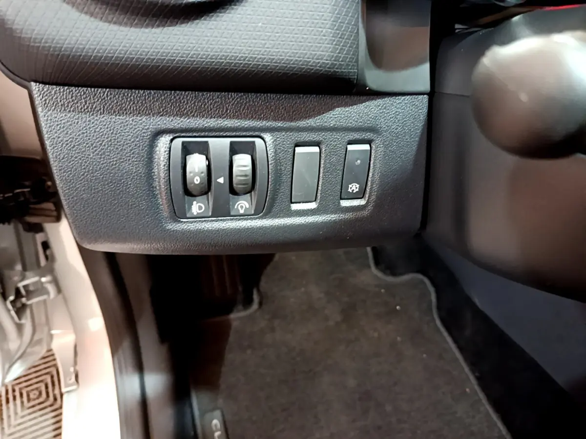 Gros plan sur les commandes de réglage des phares et antipatinage côté gauche d'une Renault Clio Business gris clair 2019.