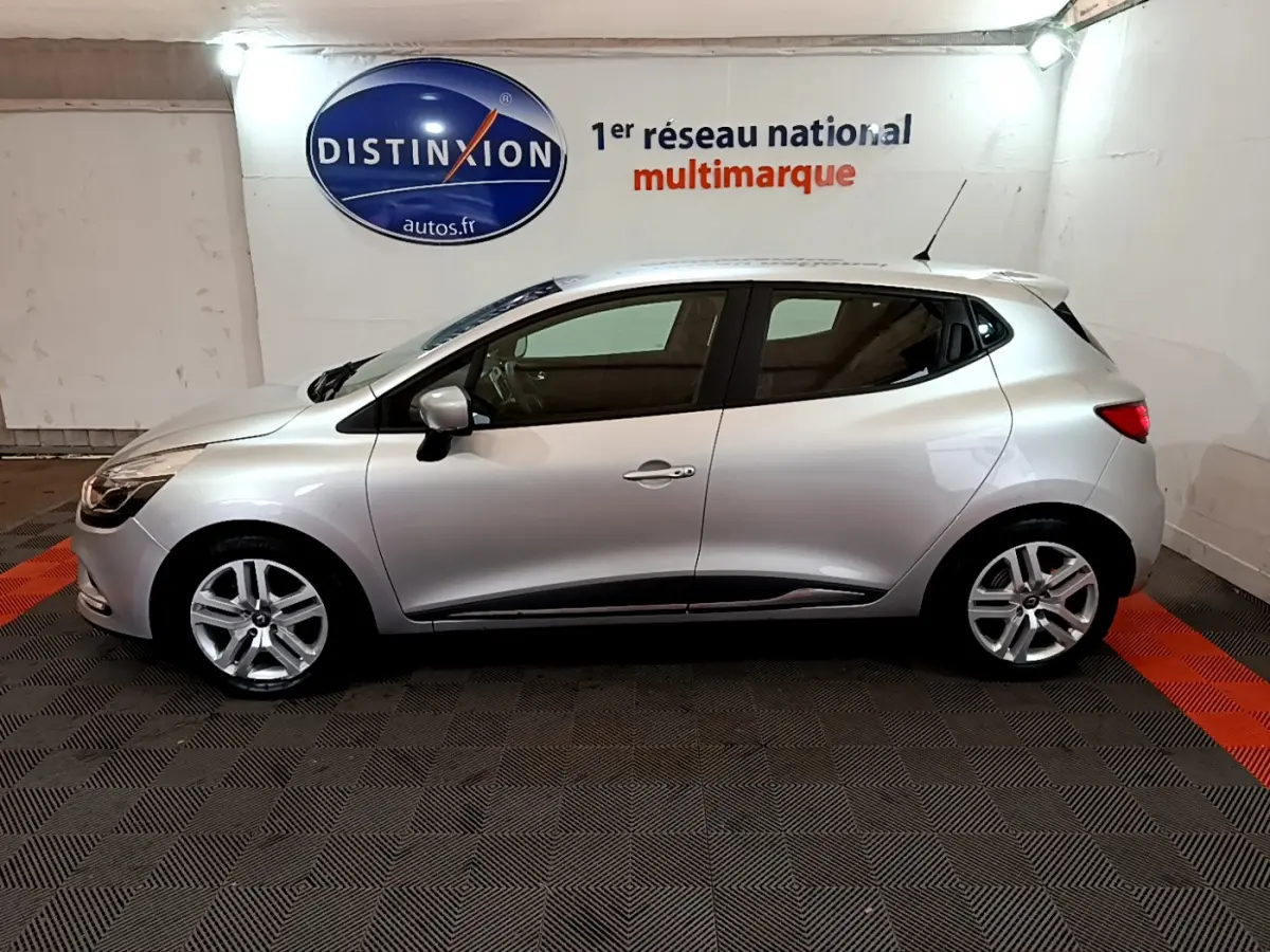 Profil côté gauche d'une Renault Clio Business TCe 90 gris clair, stationnée en intérieur sur sol noir et rouge.