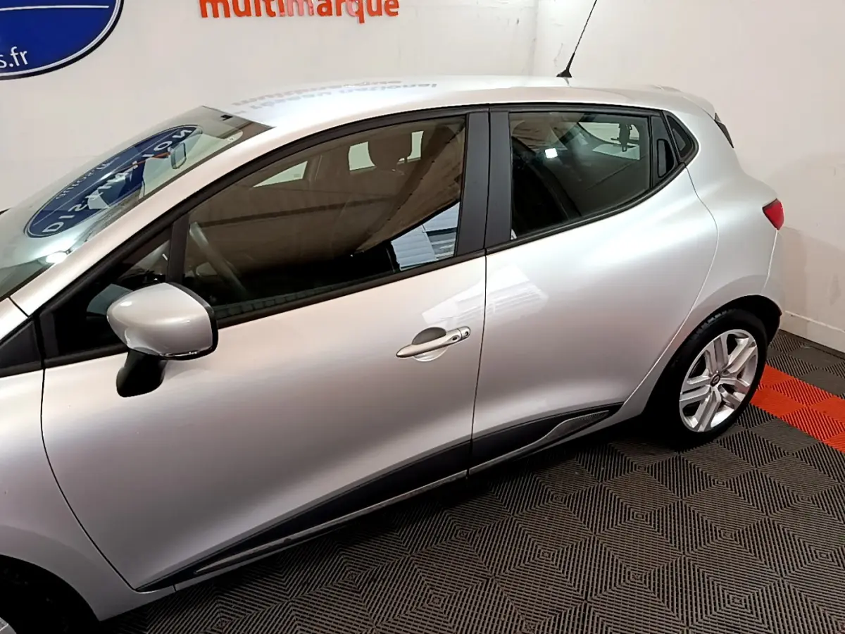 Profil côté gauche d'une Renault Clio Business TCe 90 gris clair, avec rétroviseur et poignées de porte visibles.