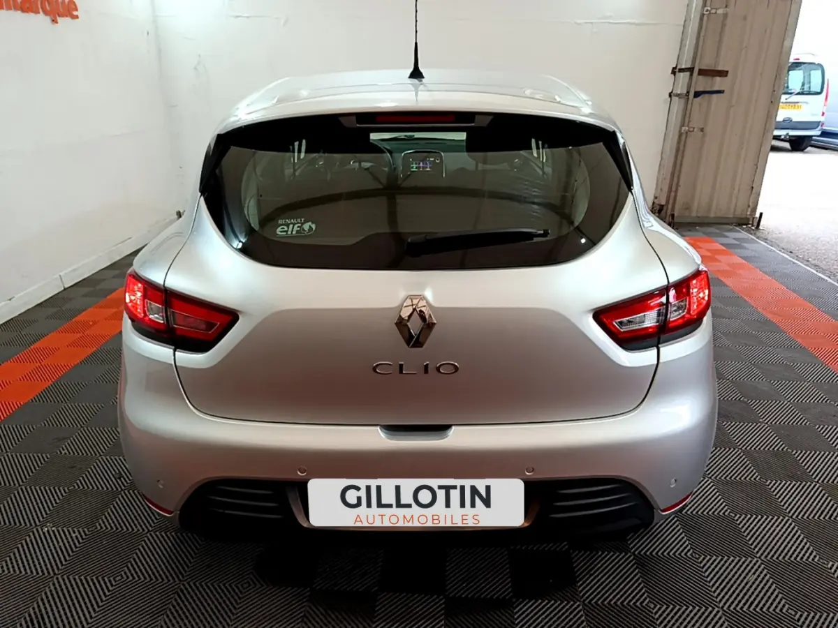 Vue arrière d'une Renault Clio gris clair 2019 avec feux arrière allumés et logo visible sur un sol à damiers noir et orange.