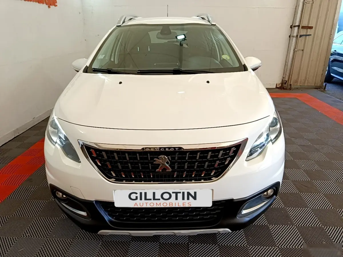 Vue avant d'un Peugeot 2008 blanc avec calandre chromée et phares allumés en intérieur showroom.