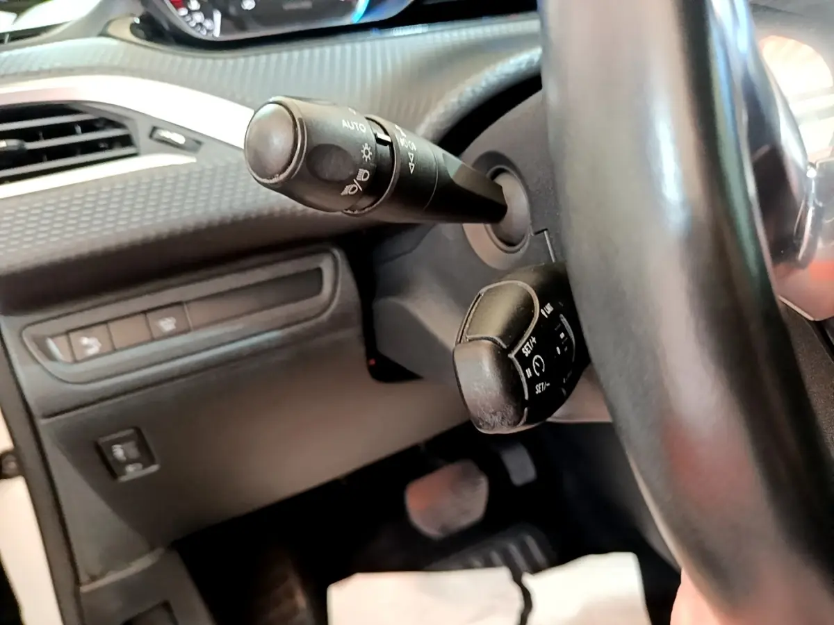 Gros plan sur la colonne de direction et commandes au volant noir du Peugeot 2008, intérieur sombre avec tableau de bord texturé.