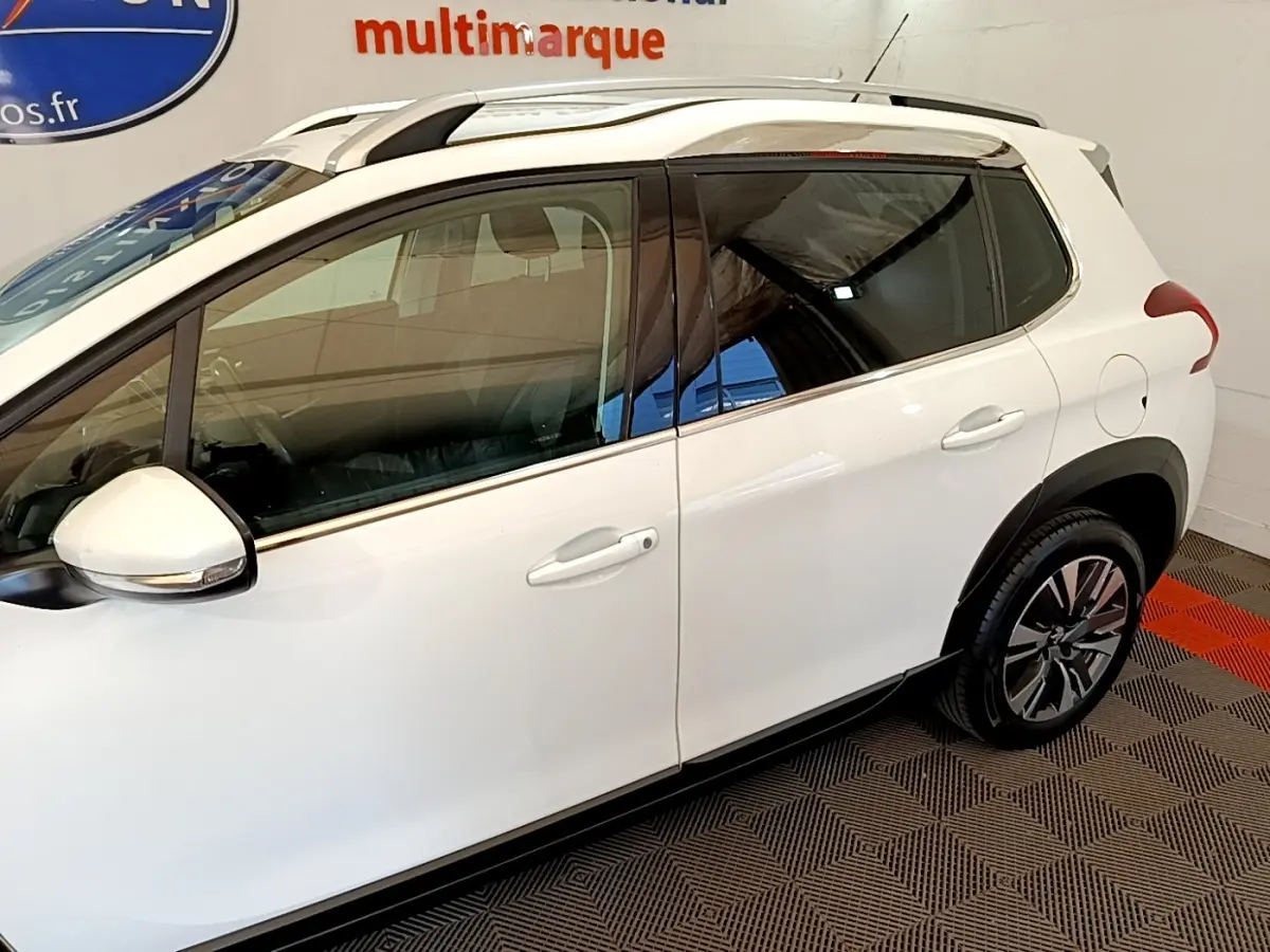 Vue côté droit du Peugeot 2008 blanc, mettant en valeur les jantes alliage et les barres de toit chromées.