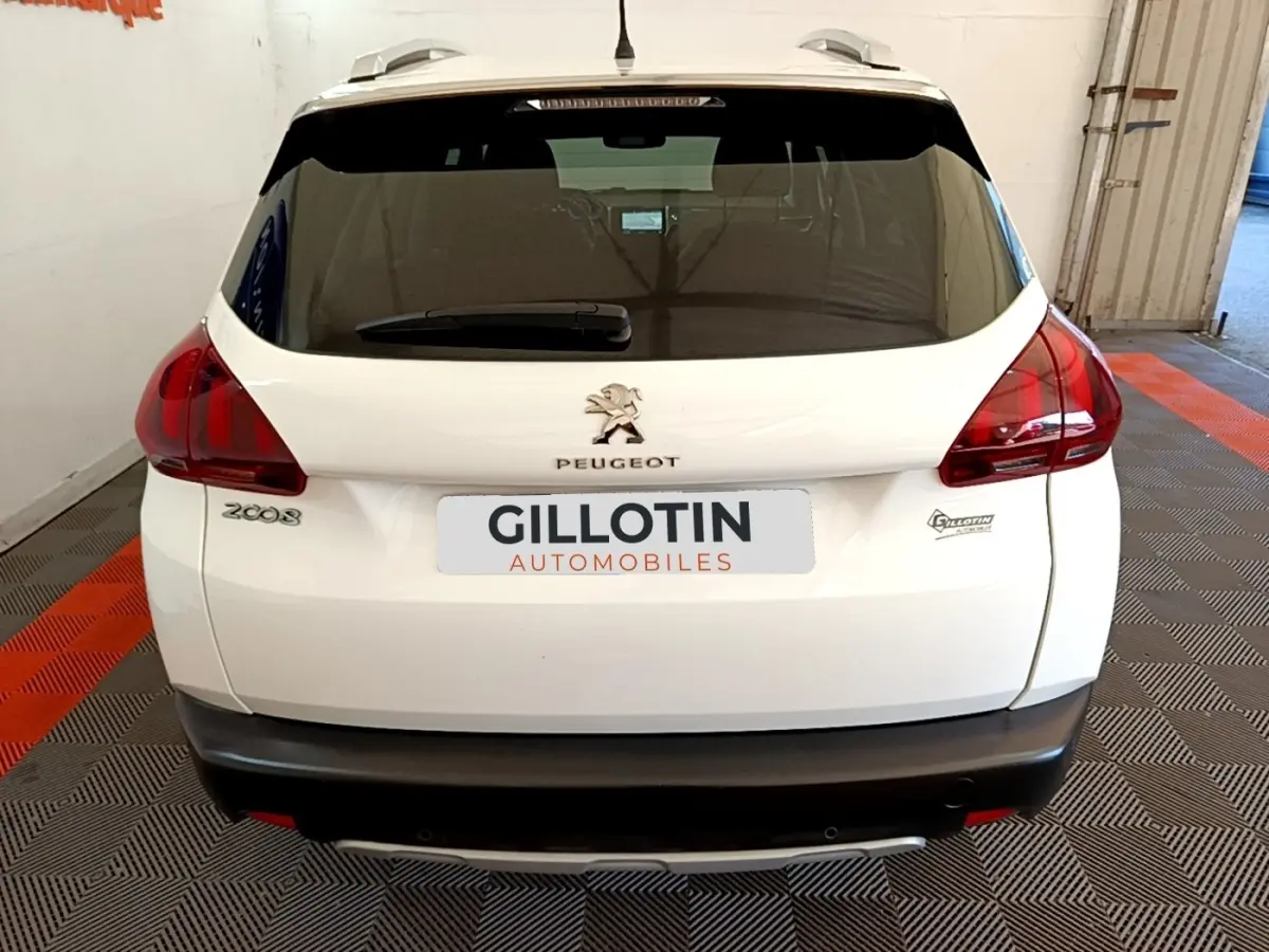 Vue arrière d'un Peugeot 2008 blanc avec feux arrière rouges et logo Peugeot visible sur un sol à damier noir et orange.