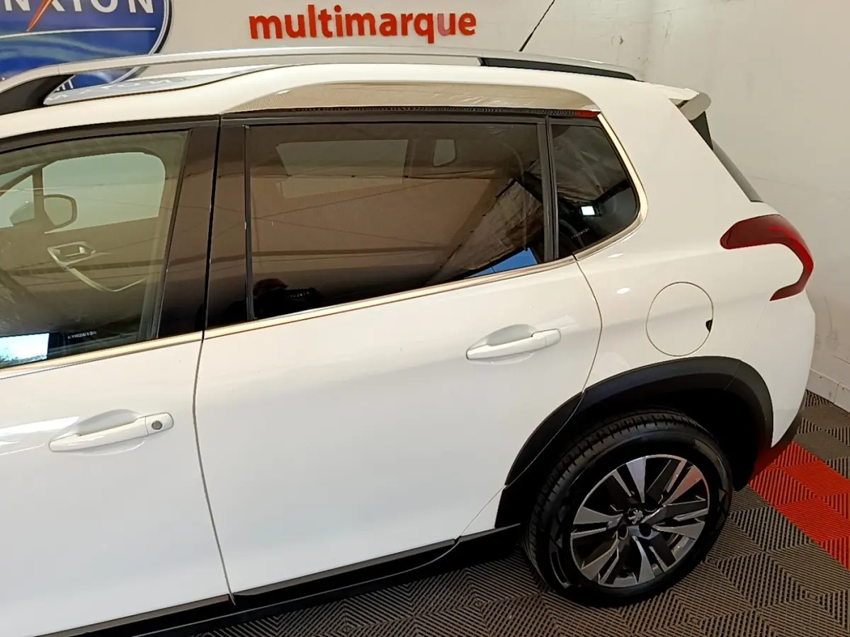 Vue côté gauche arrière du Peugeot 2008 blanc avec jantes alliage et vitres teintées en intérieur showroom.