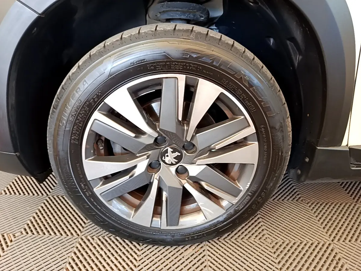 Gros plan sur la roue galette acier grise avec logo Peugeot, côté avant droit du véhicule blanc.