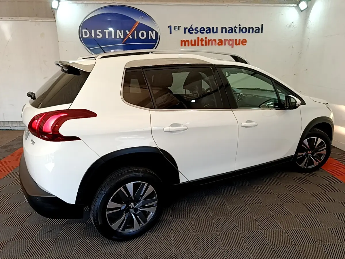 Peugeot 2008 blanc vue de profil droit en intérieur, avec jantes alliage et barres de toit chromées.