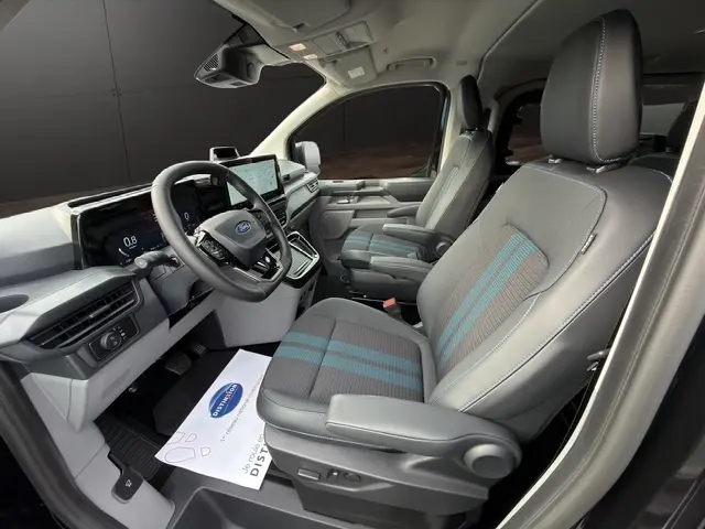 Vue intérieure côté conducteur du Ford Transit Fourgon noir 2026, montrant sièges tissu avec surpiqûres bleues et tableau de bord digital.