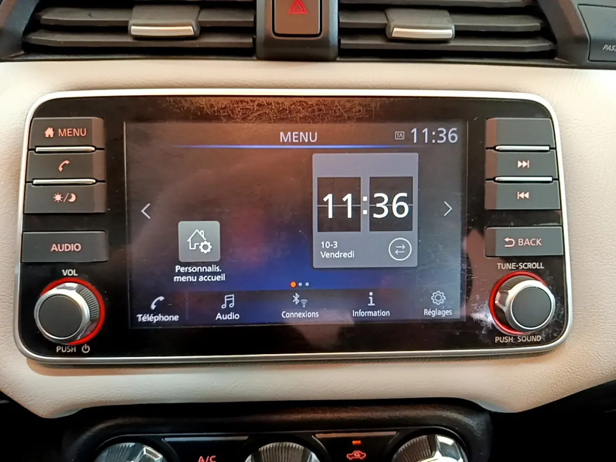 Écran tactile central du tableau de bord beige de la Nissan Micra IG-T 92 Acenta 2022 affichant l'heure et le menu principal.