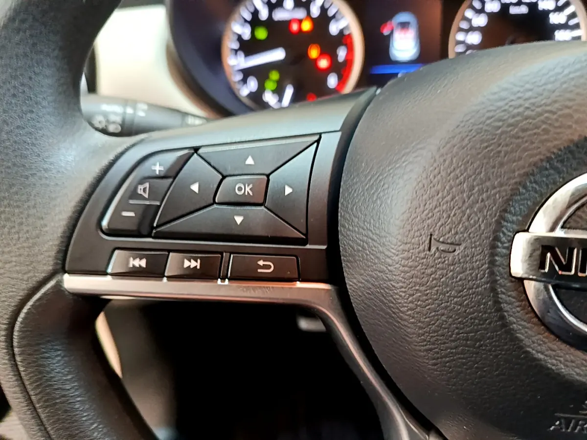 Gros plan sur le côté gauche du volant noir de la Nissan Micra 2022 avec commandes multifonctions et logo Nissan visible.