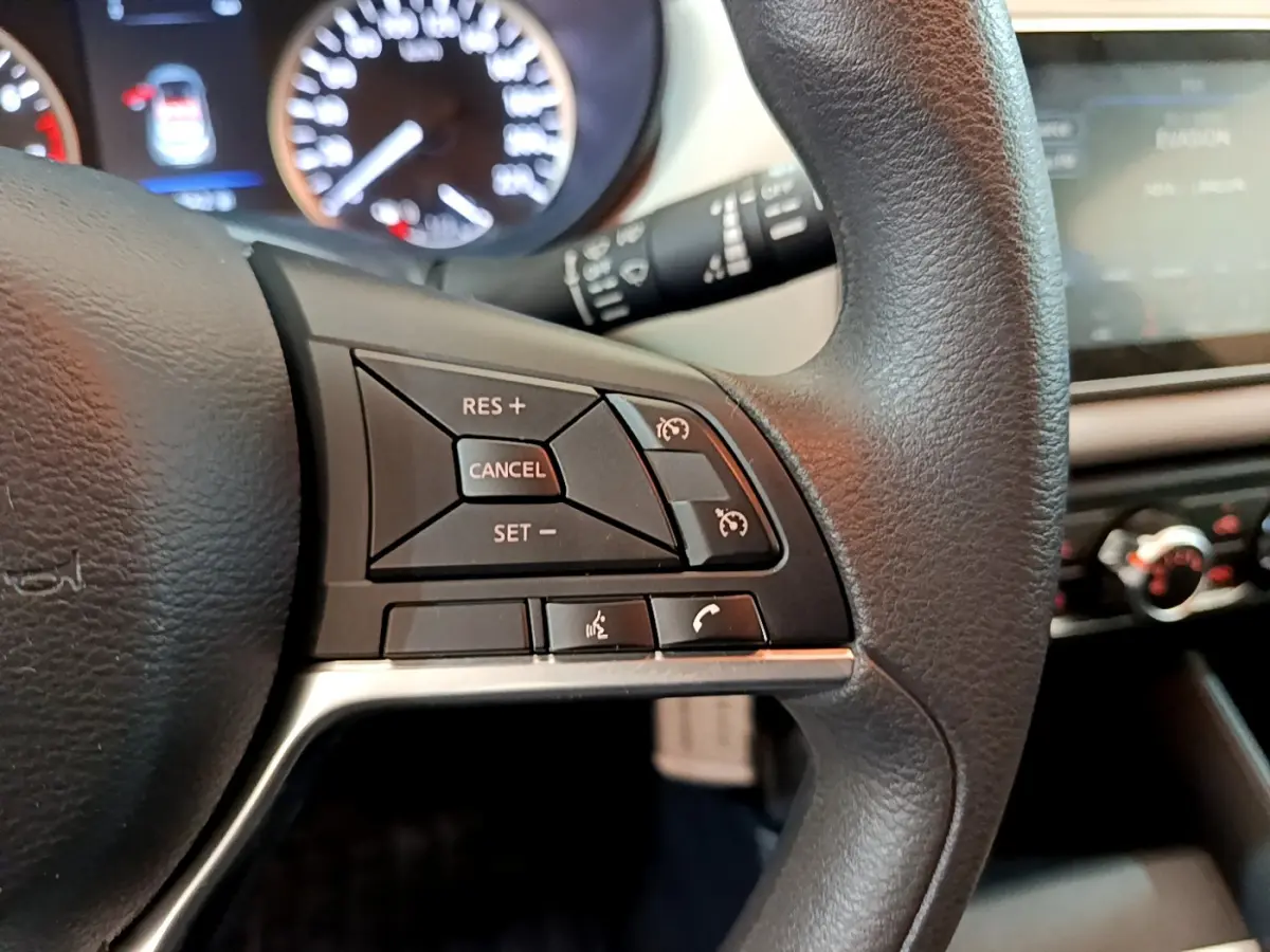 Gros plan sur les commandes du volant à droite dans l'habitacle d'une Nissan Micra blanche 2022, avec tableau de bord flou.