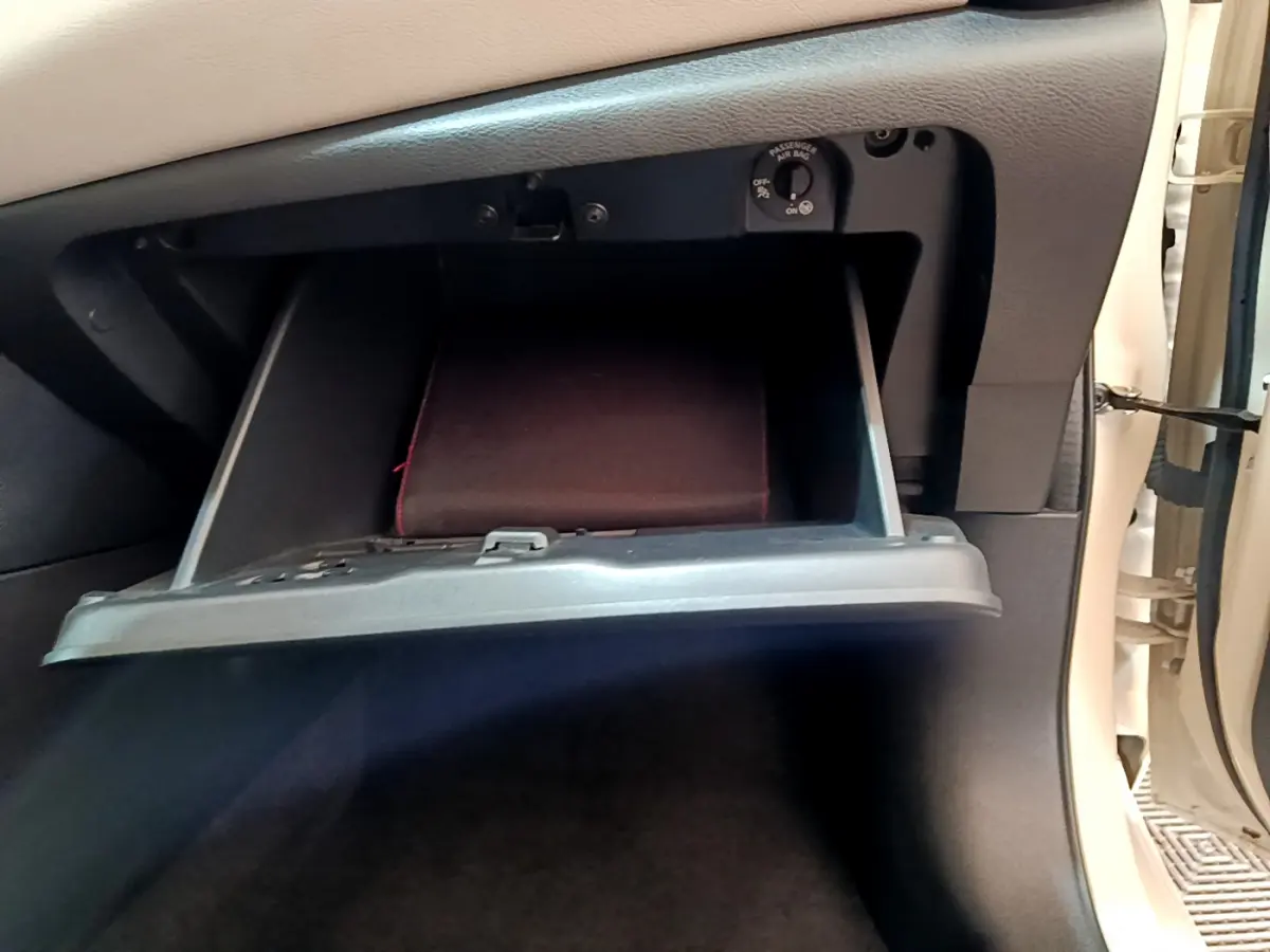 Gros plan sur la boîte à gants ouverte côté passager d'une Nissan Micra blanche, avec un manuel à l'intérieur.