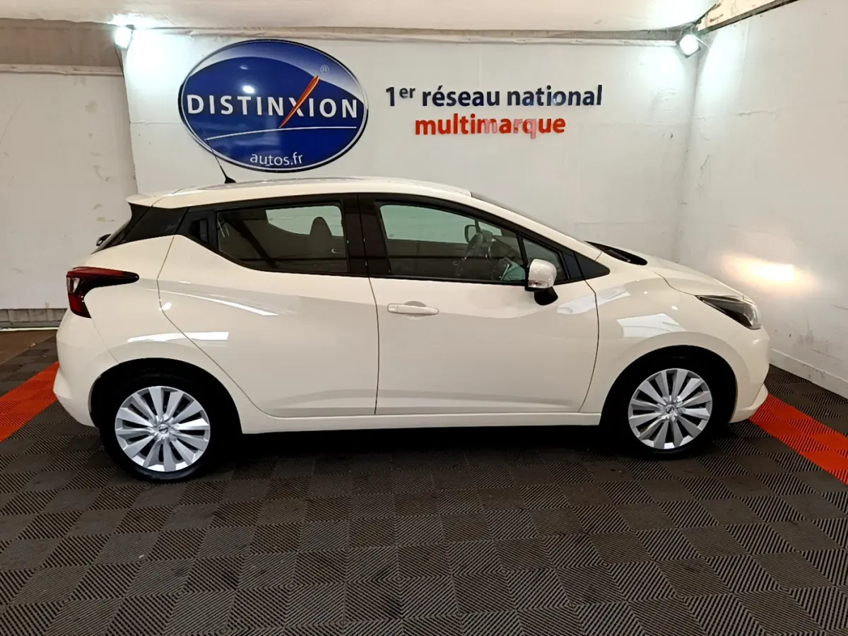 Profil côté droit d'une Nissan Micra IG-T 92 Acenta blanche 2022 dans un showroom avec logo Distinxion en arrière-plan.
