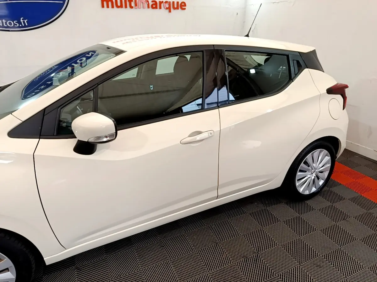 Profil côté gauche d'une Nissan Micra IG-T 92 Acenta blanche, avec rétroviseur et jante visibles sur fond intérieur.