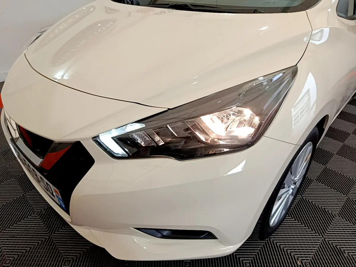 Vue 3/4 avant droit d'une Nissan Micra IG-T 92 Acenta blanche avec phares LED allumés et calandre noire distinctive.