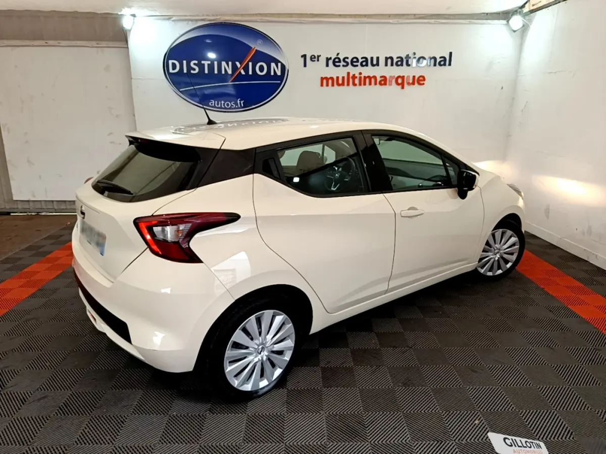 Vue 3/4 arrière droite d'une Nissan Micra blanche 2022 dans un showroom avec logo Distinxion en arrière-plan.