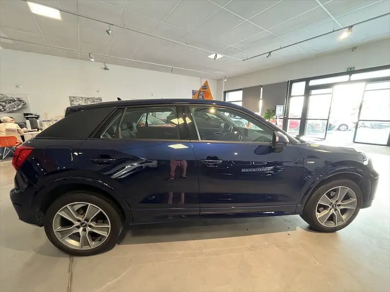 Profil côté gauche d'un Audi Q2 30 TFSI S-Line bleu Navarre métal, avec jantes alliage et toit noir en showroom.