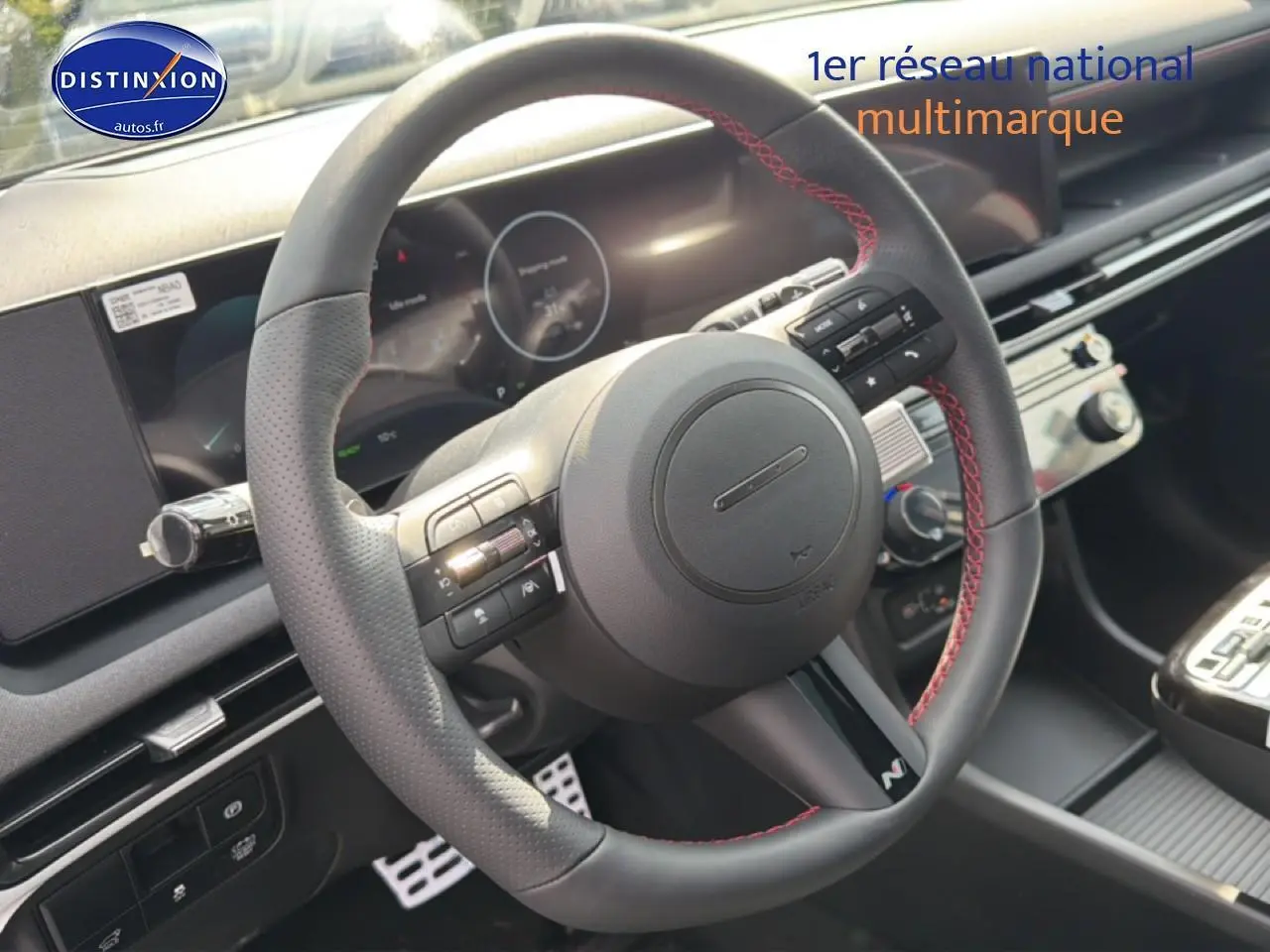 Vue rapprochée du volant cuir noir avec surpiqûres rouges du Hyundai Tucson 2026, tableau de bord et écran tactile visibles.