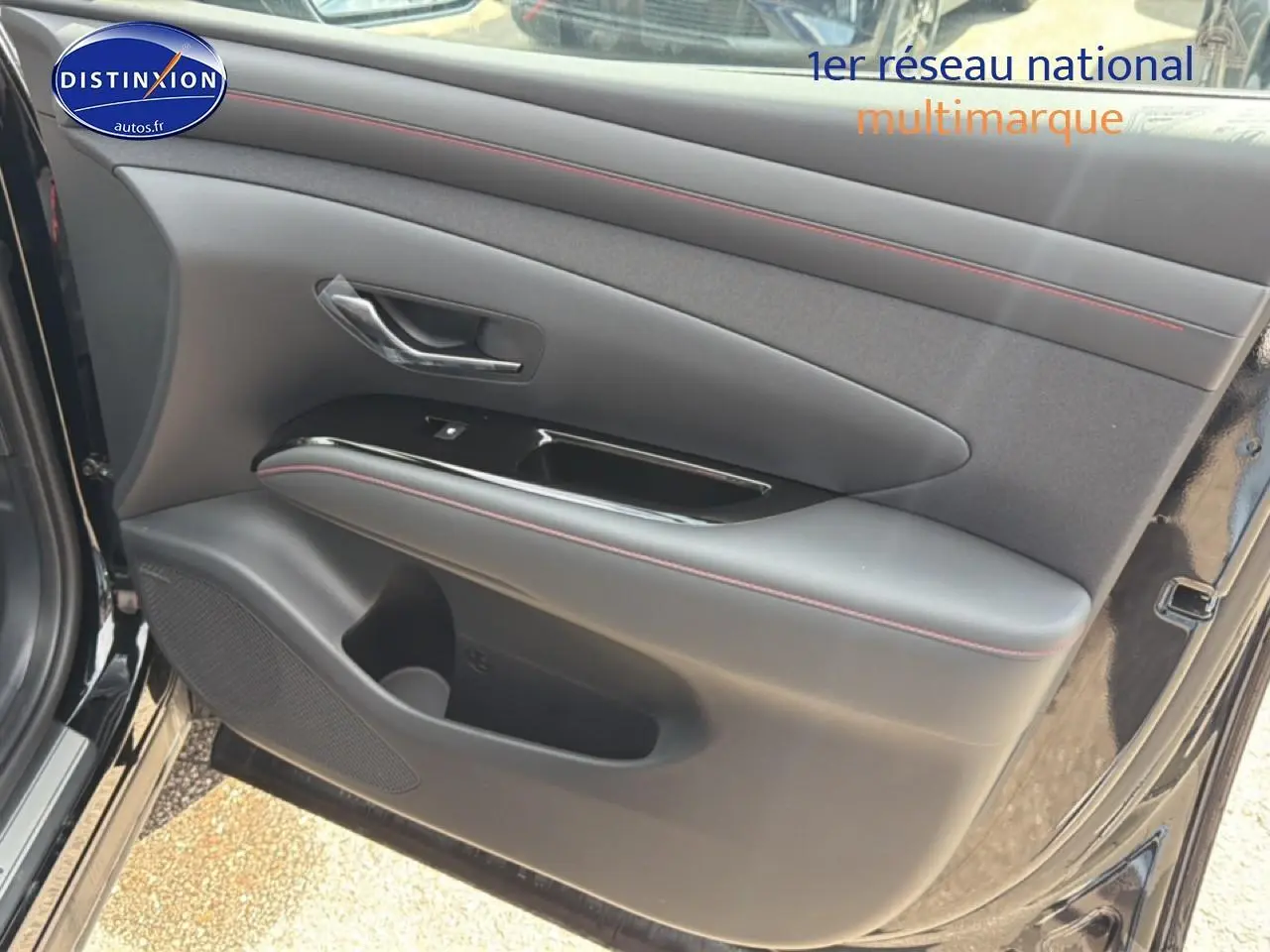 Vue rapprochée de la porte avant gauche noire du Hyundai Tucson 2026 avec surpiqûres rouges et poignée chromée.