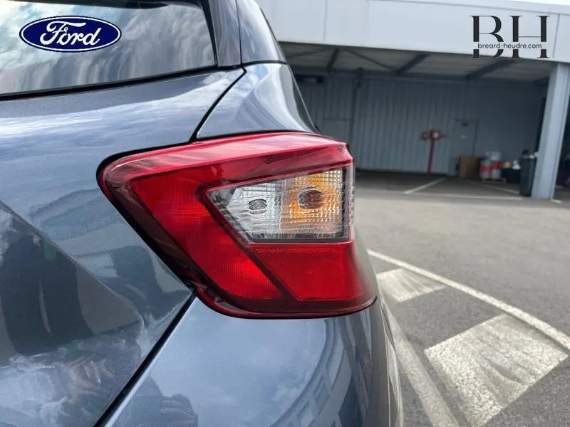 Gros plan sur le feu arrière droit d'une Nissan Micra gris acier, avec reflet métallique sous lumière naturelle.