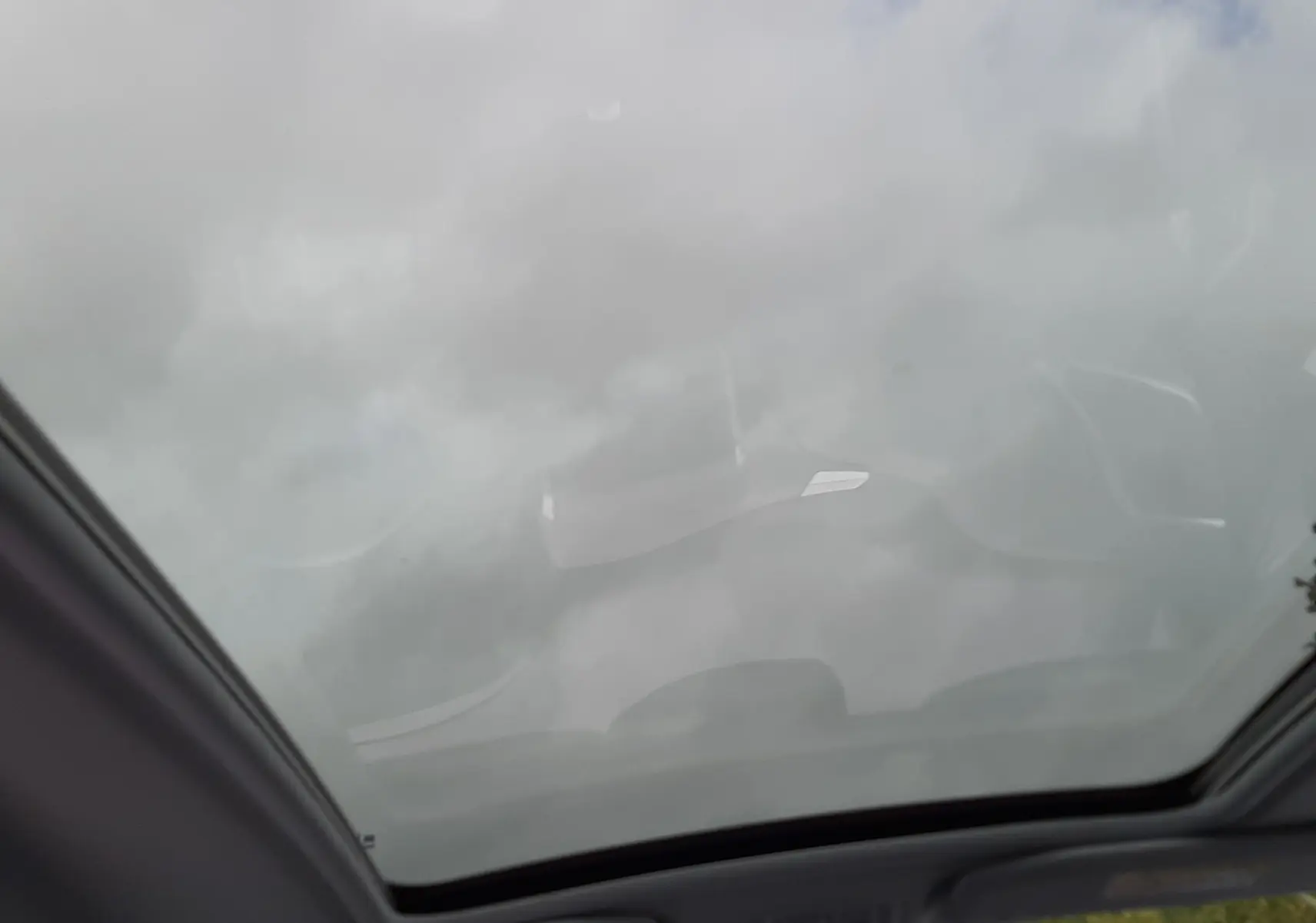 Vue intérieure du toit panoramique vitré du Peugeot 2008 blanc, offrant une ouverture sur un ciel nuageux.