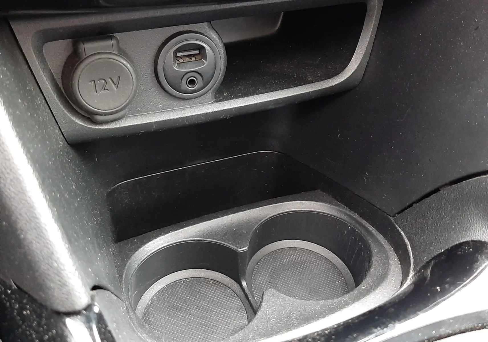 Gros plan sur la console centrale noire du Peugeot 2008 2017 montrant prise 12V, port USB et porte-gobelets.