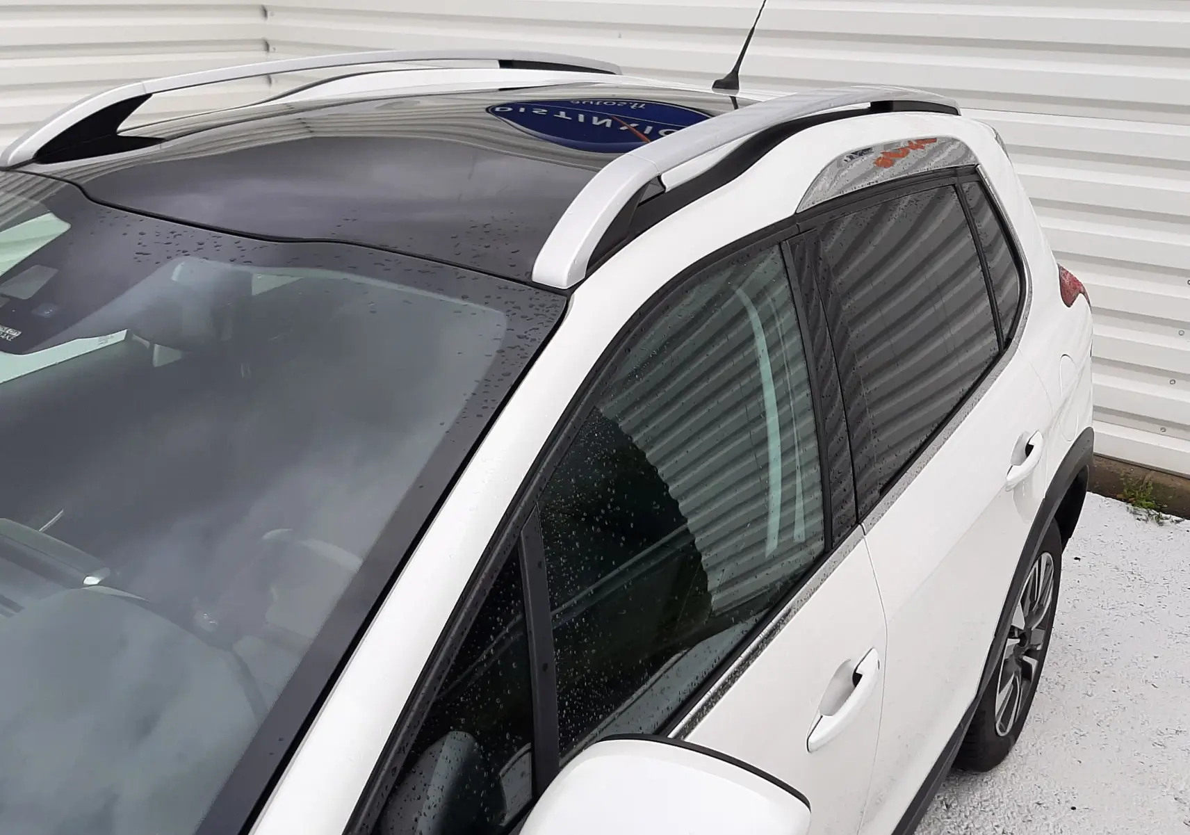 Vue 3/4 avant droit du Peugeot 2008 blanc avec toit panoramique noir et barres de toit argentées.