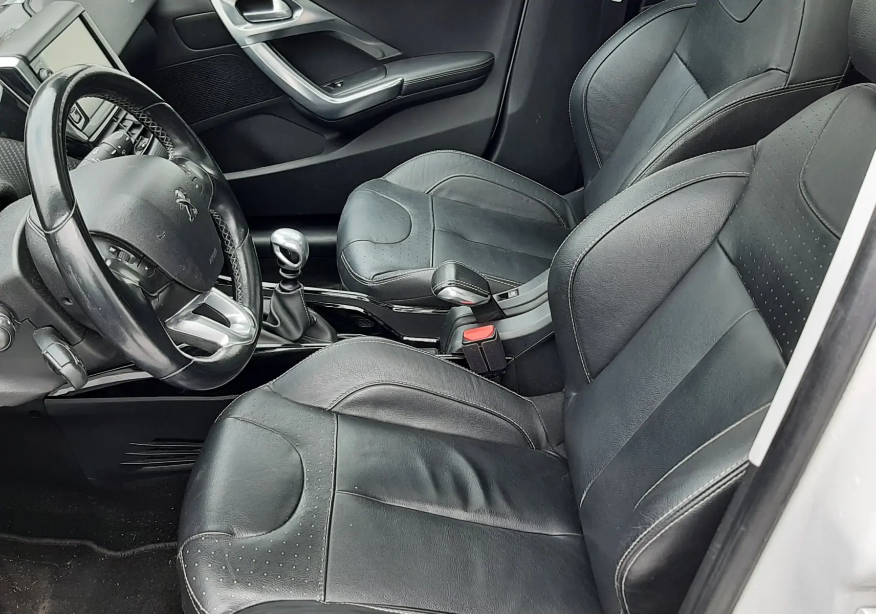 Vue intérieure côté conducteur du Peugeot 2008 blanc de 2017, sièges en cuir noir et volant multifonction.