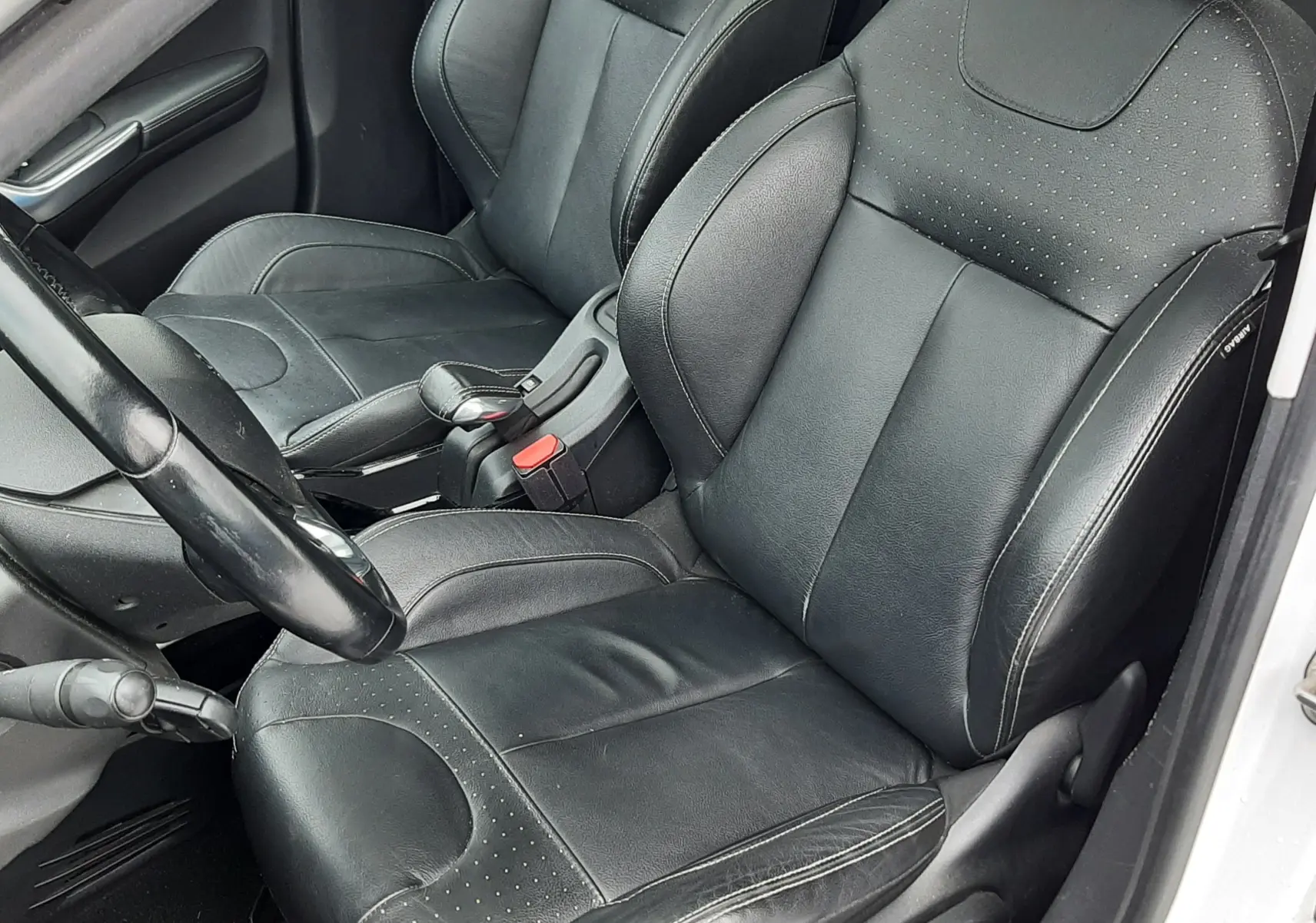 Vue intérieure côté conducteur du Peugeot 2008 blanc de 2017, sièges en cuir noir avec coutures apparentes.