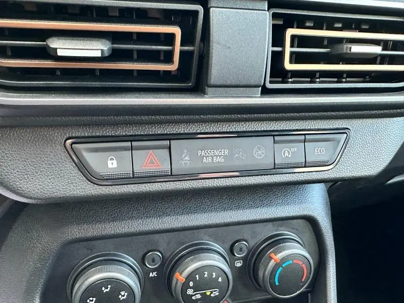 Tableau de bord noir de Dacia Sandero blanc, avec commandes climatisation et boutons de sécurité visibles.