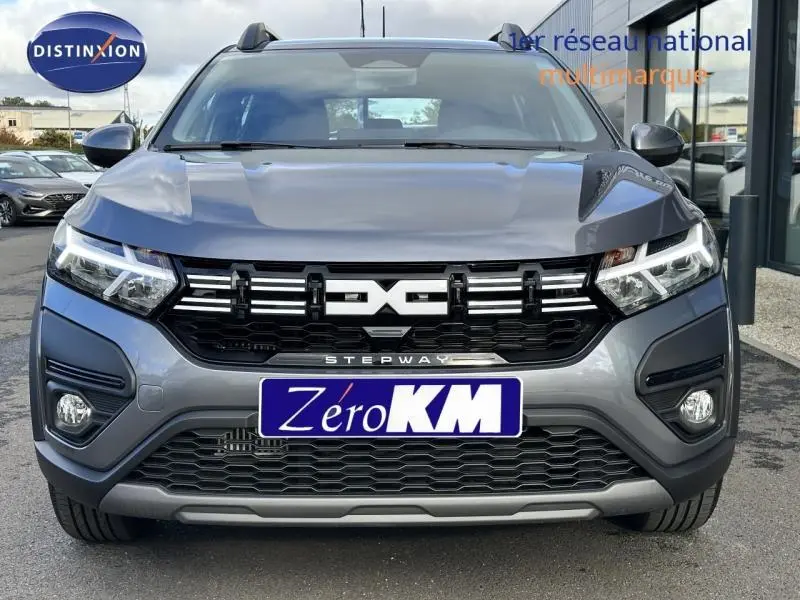 Vue frontale d'un Dacia Sandero Stepway gris métallisé avec calandre noire et phares LED allumés.