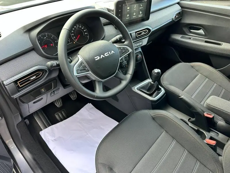Intérieur avant droit de la Dacia Sandero blanche 2025, volant multifonction, boîte manuelle et sièges tissu Expression noirs.