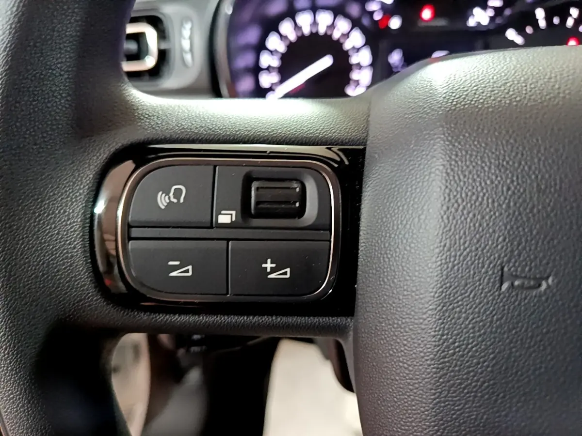 Gros plan sur les commandes du volant à gauche de la Citroën C3 blanche, tableau de bord flou en arrière-plan.