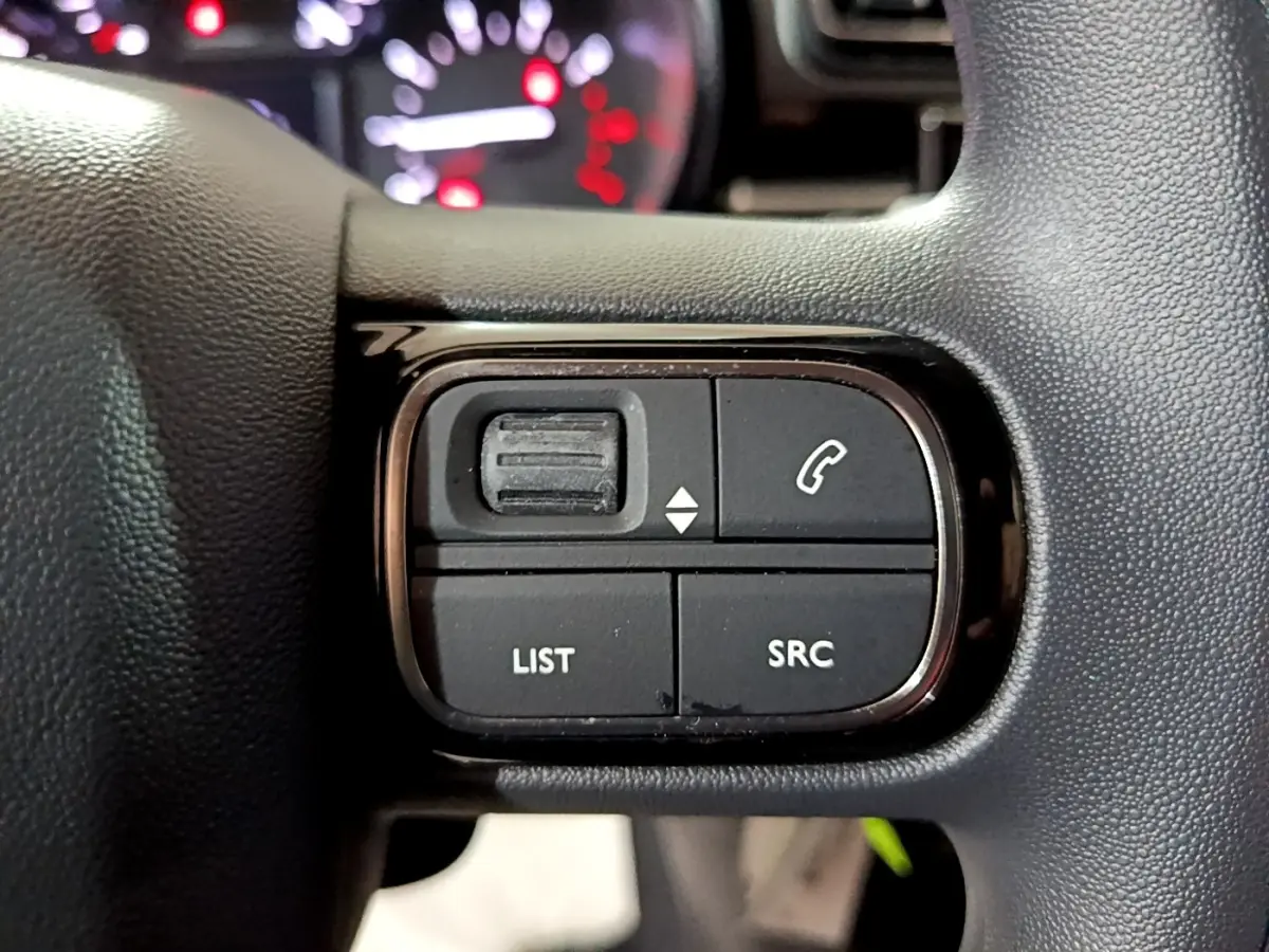 Gros plan sur les commandes du volant noir de la Citroën C3 PureTech 83 Shine 2023, boutons LIST et SRC visibles.