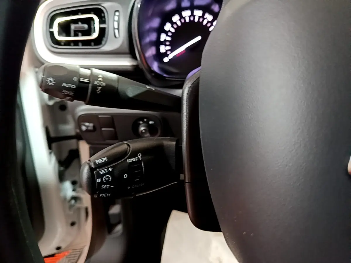 Gros plan sur la commande de régulateur de vitesse à gauche du volant dans l'habitacle d'une Citroën C3 blanche.