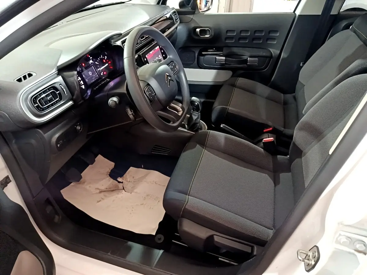 Intérieur côté conducteur d'une Citroën C3 blanche 2023, volant multifonctions, tableau de bord digital et sièges tissu noirs.