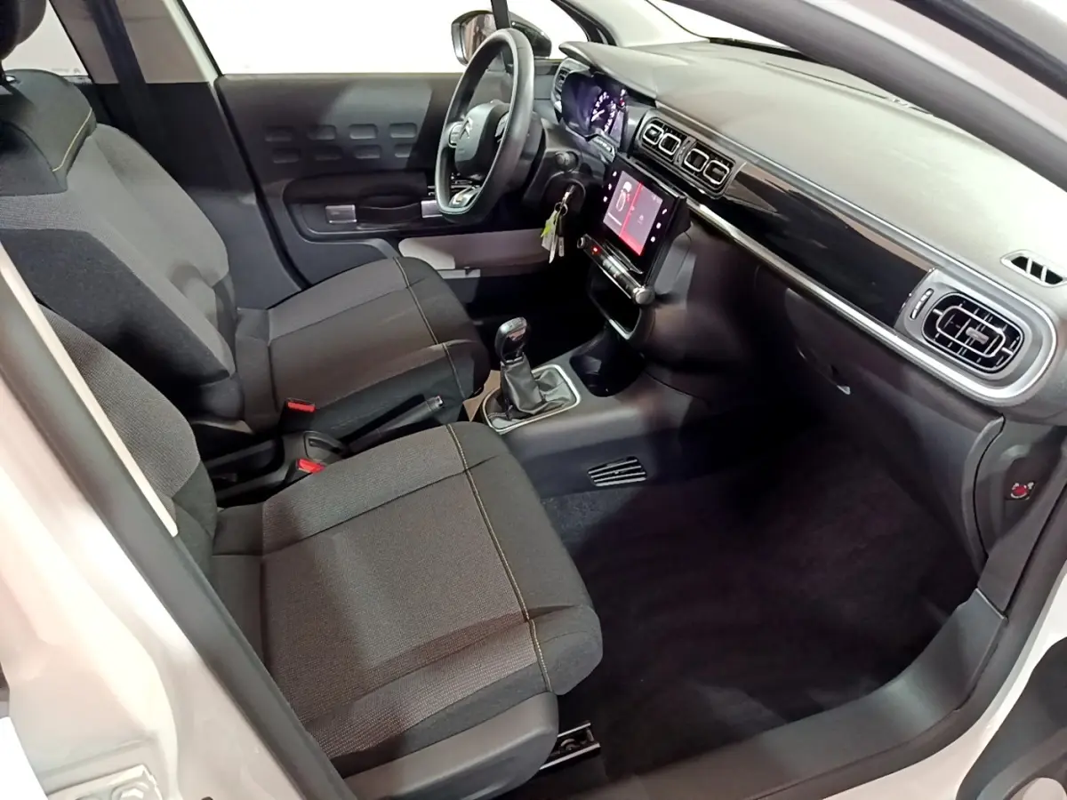 Vue intérieure côté conducteur de la Citroën C3 blanche 2023 avec tableau de bord noir et écran tactile central.