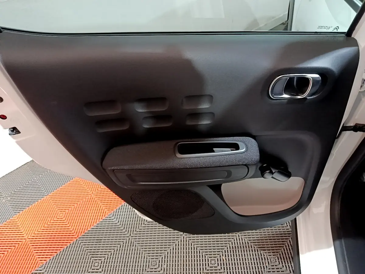 Porte intérieure côté gauche noire et grise de la Citroën C3 blanche 2023, avec poignée chromée et commande de vitre manuelle.