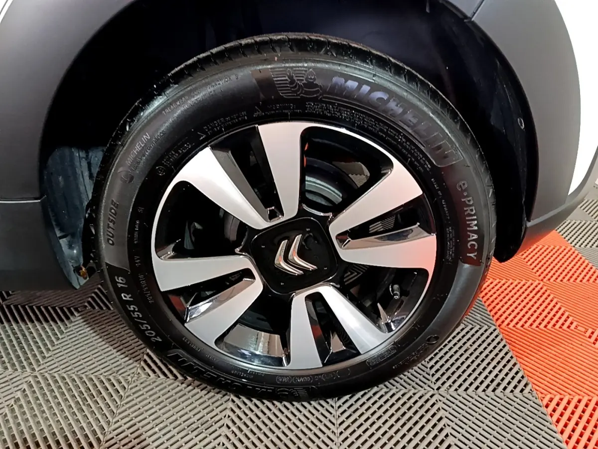 Gros plan sur la jante alliage noire et argentée d'une Citroën C3 blanche, roue avant droite visible.