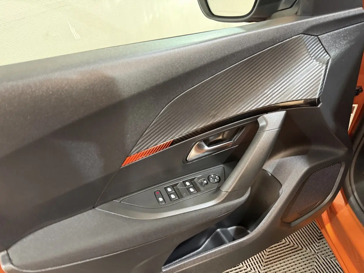 Détail de la porte avant gauche du Peugeot 2008 orange 2022 avec insert effet carbone et commandes électriques.